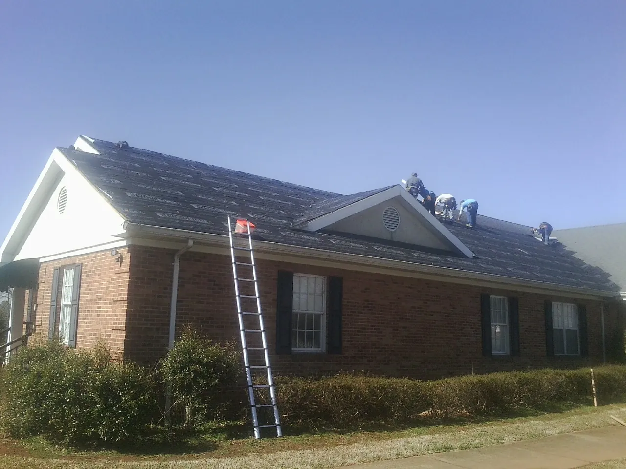 Crew tearing shingles off a brick ranch roof with a ladder set — Metal Roof Repair work by our crew in Eupora
