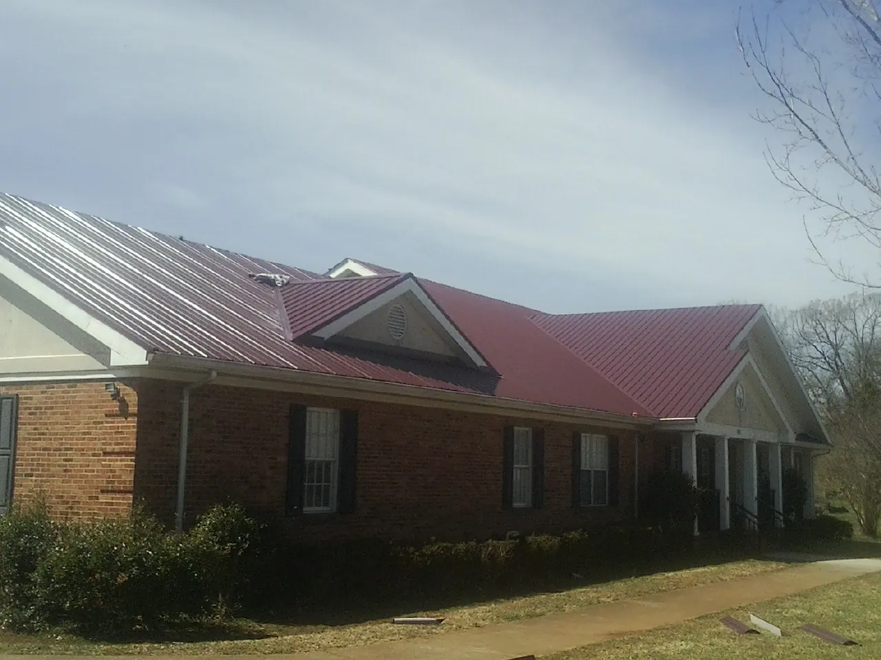 Red metal roof with gabled entries on a long brick building, from a Hail Damage Roof Repair job in Eupora