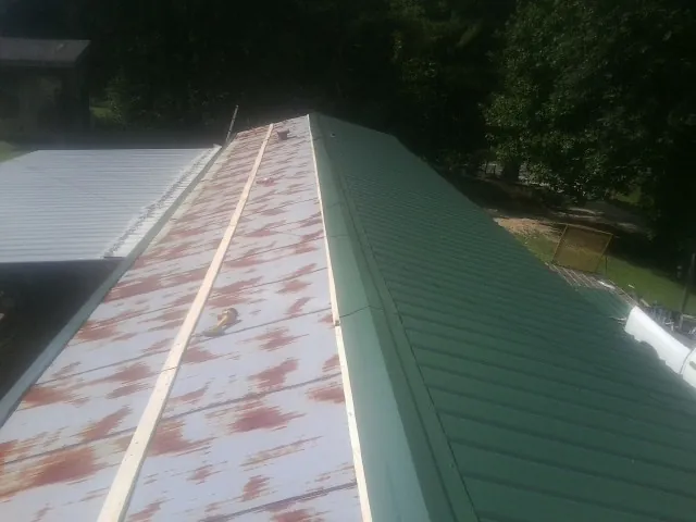 Old rusted panels beside newly installed green metal roofing — Wind Damage Roof Repair by Roofing Brothers in Eupora