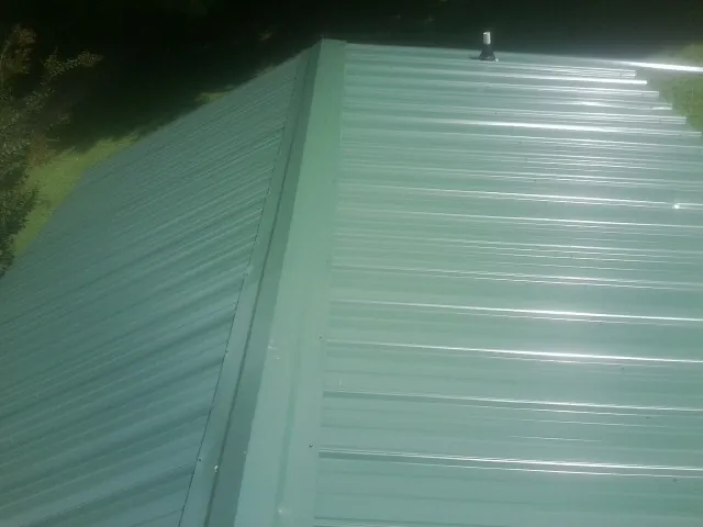 New green metal panels meeting at the ridge of a roof — Flat Roof Repair work by our crew in Eupora