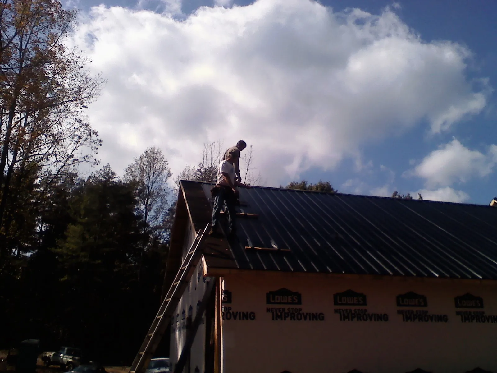 Roofer fastening dark metal panels high against a cloudy sky, from a Roof Inspection job in Eupora