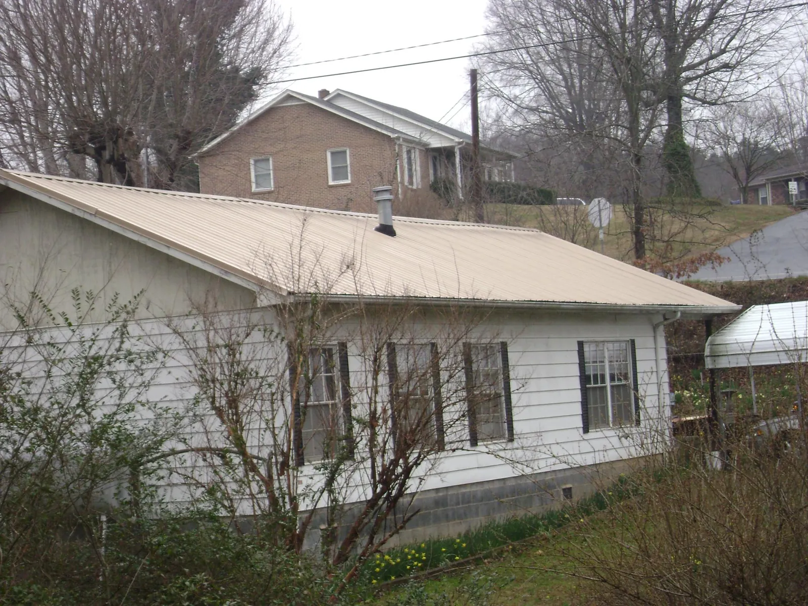 Tan metal roof on a white sided house set into a hillside — Commercial Roofing by Roofing Brothers in Eupora